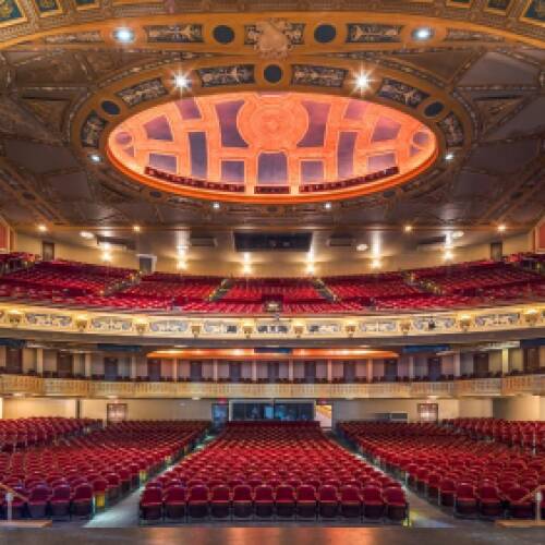Interior of an ornate theater with rows of red seats, balconies, and a domed ceiling